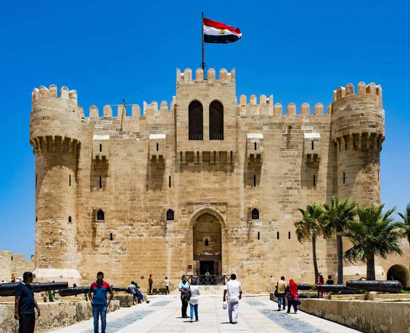 Haupttor und Türme der Zitadelle des Qaitbay mit Flagge und Besuchern auf dem Zugang