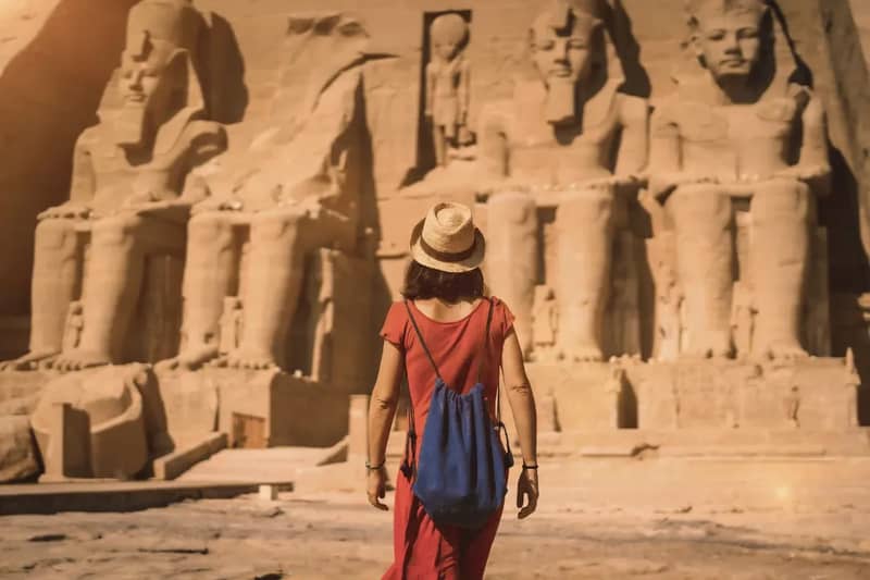 Femme en chapeau de soleil et robe rouge face aux statues colossales d'Abou Simbel