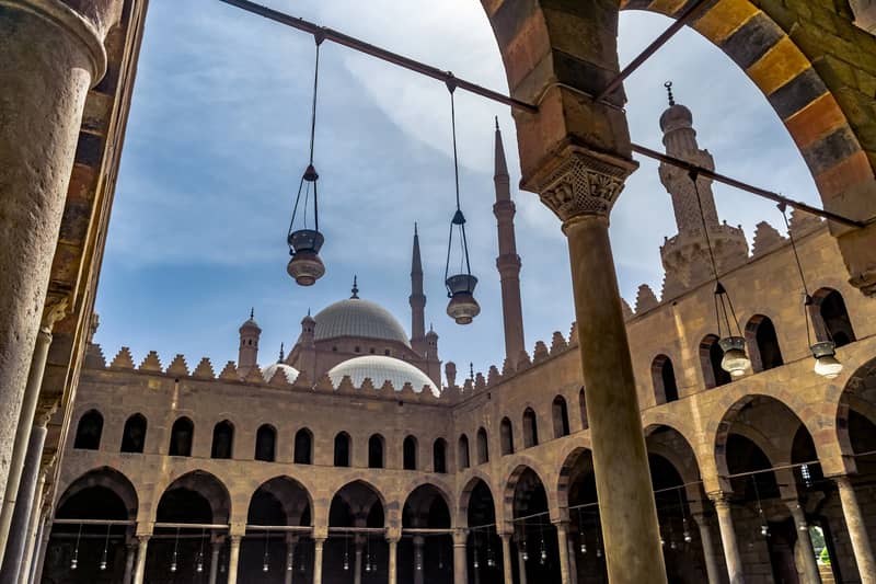 Arcades and hanging lamps at the Cairo Citadel, with the Muhammad Ali Mosque dome behind