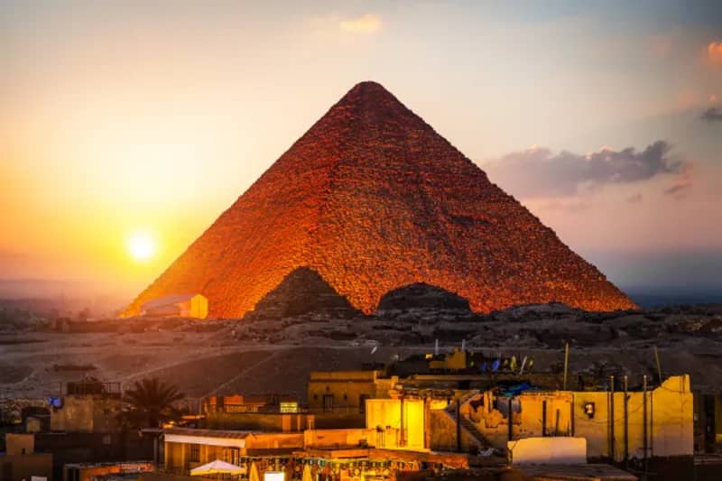 Pyramide du plateau de Gizeh éclairée par le soleil couchant, au-dessus des maisons en bordure du plateau