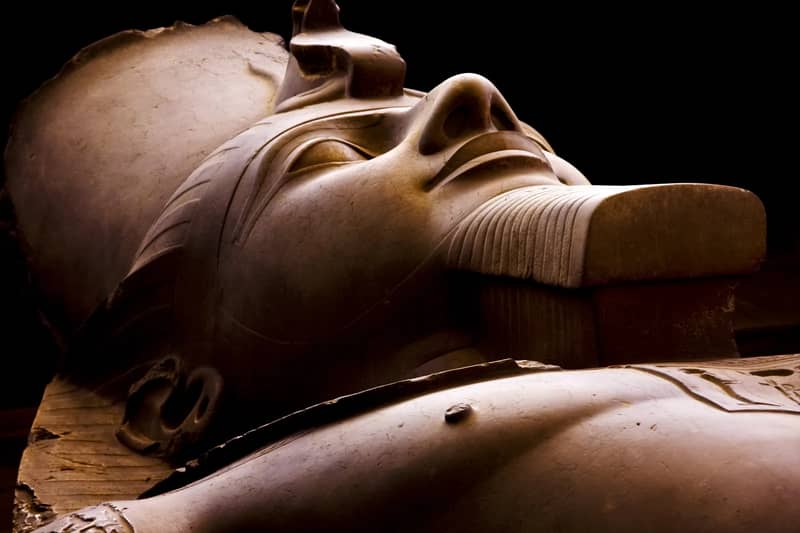 Gesicht der liegenden Kolossalstatue Ramses' II. aus Kalkstein in Memphis, beleuchtet vor dunklem Hintergrund
