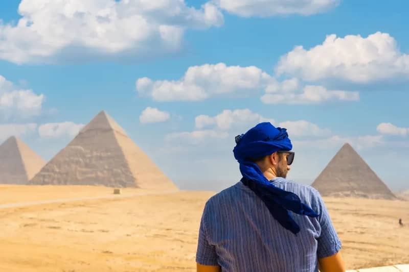 Personne coiffée d'un foulard bleu regardant les pyramides de Gizeh