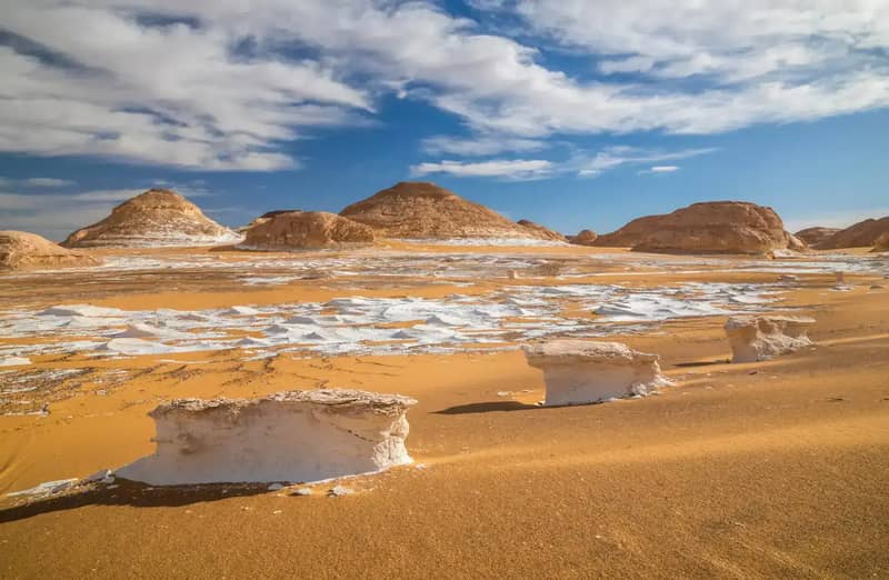 White chalk rocks scattered across the sand of the White Desert under a blue sky