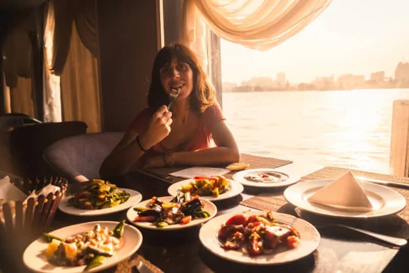 Frau beim Essen an einem gedeckten Fenstertisch mit mehreren Tellern, dahinter die Skyline einer Stadt