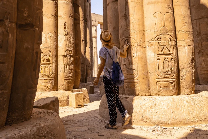 A joyful visitor touching the ancient columns in Luxor Temple, embracing the beauty of Egypt's heritage with DMC Egypt.