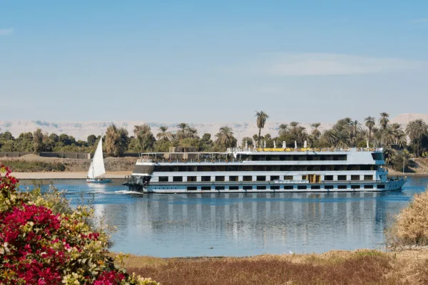 Enjoy the beauty of Egypt: Nile cruise boat sailing on the Nile River with a traditional felucca visible in the background, thanks to DMC Egypt.